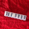 Rainbow Squared Year 5, Piece Twenty-Eight: 7. Red Black White by Rachel Cassandra. A stop-motion photo animation loop of a red background with a clear plastic pill organizer on top of it with seven slots for the days of the week filled with black pills and white pills, where the lids dance open and shut and the pills dance out of the containers and then back into the containers.